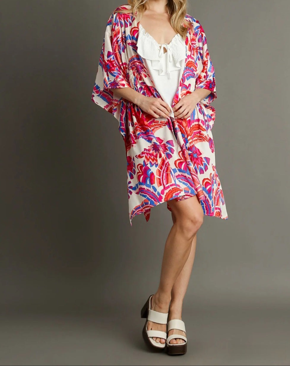 Woman wearing a colorful floral kimono over a white top on a gray background