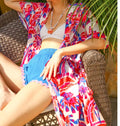 Woman sitting on a wicker chair wearing a colorful floral cover-up and blue shorts.