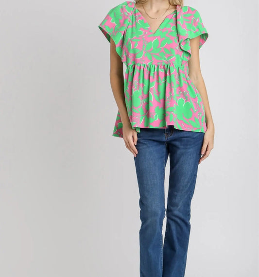 Woman wearing a pink and green floral top with blue jeans on a gray background