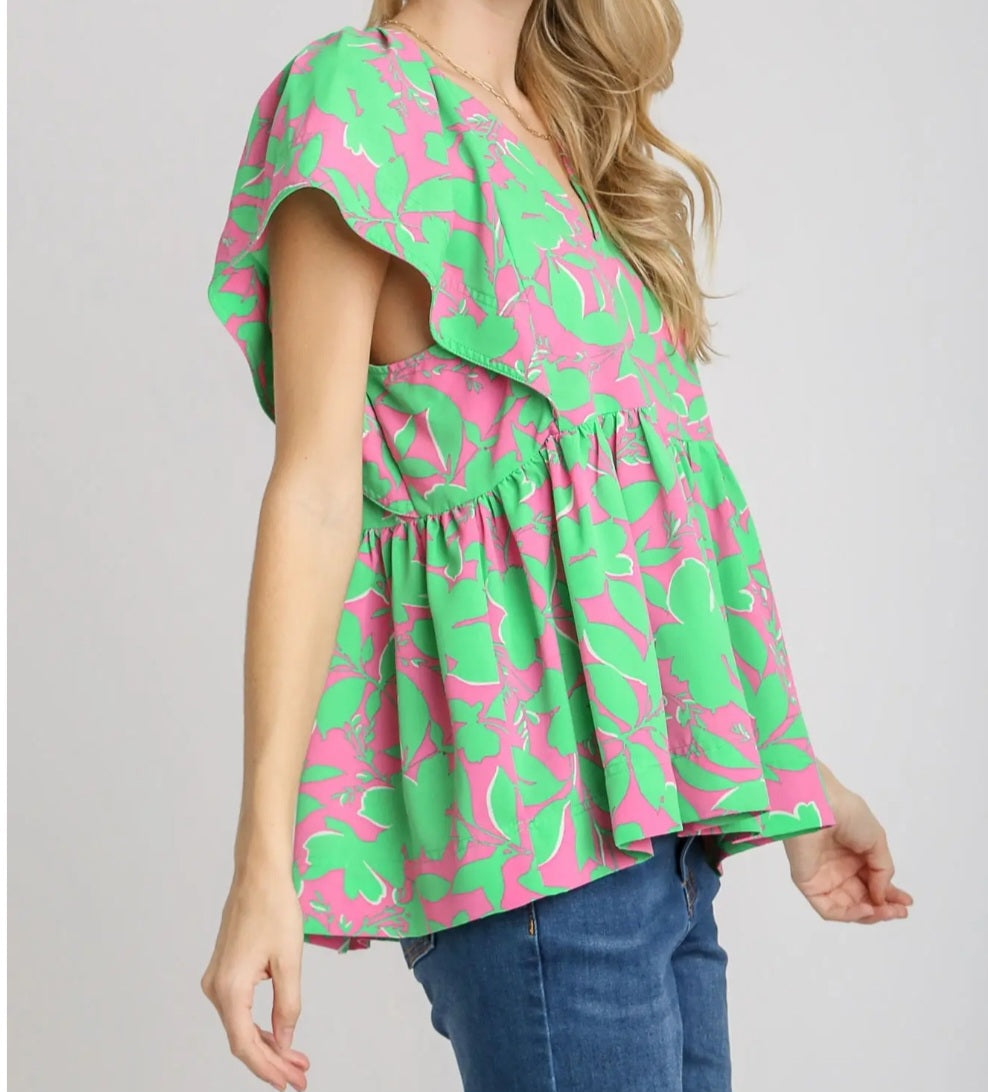 Woman wearing a green and pink patterned top with blue jeans on a plain background