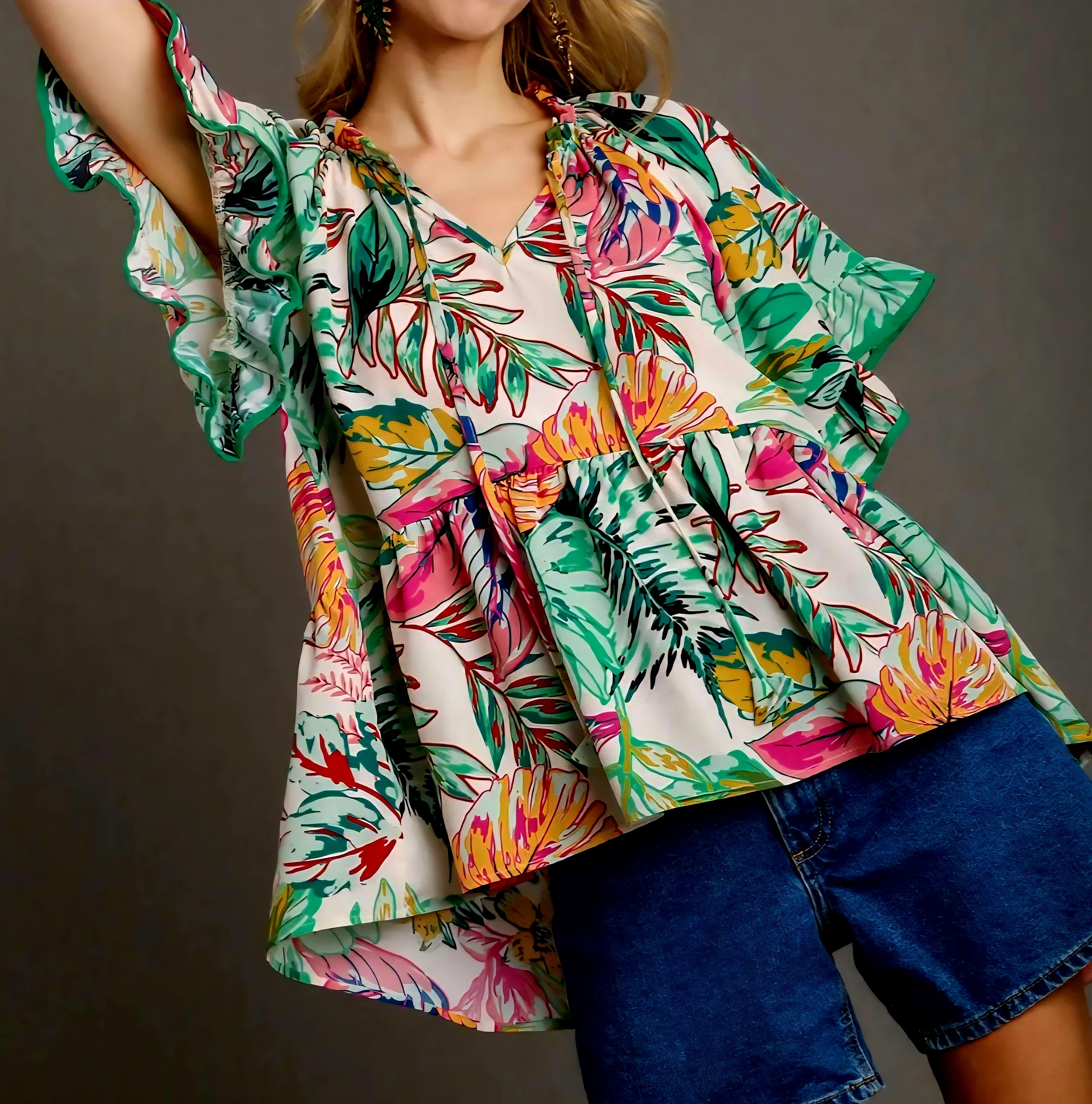 Woman wearing a colorful tropical patterned blouse with ruffled sleeves against a gray background
