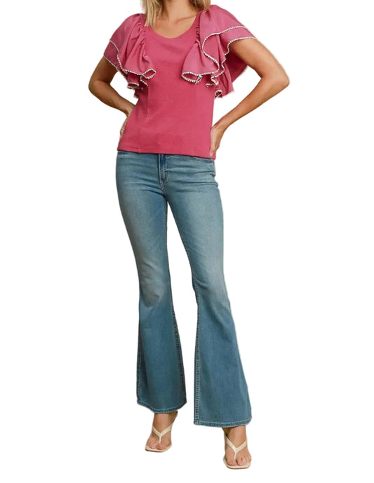 Woman wearing a pink top with ruffled sleeves and blue jeans on a beige background