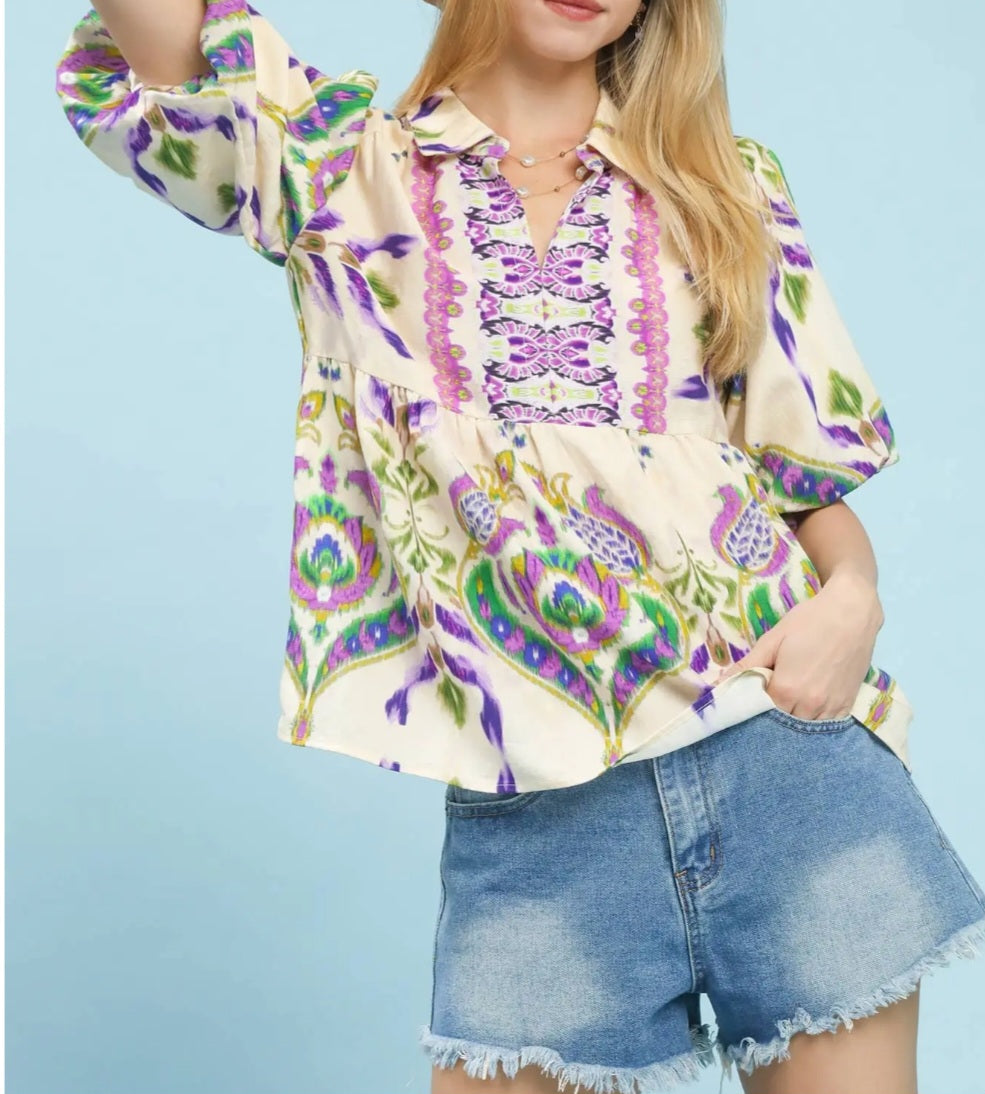 Woman wearing a colorful patterned blouse and denim shorts against a light blue background