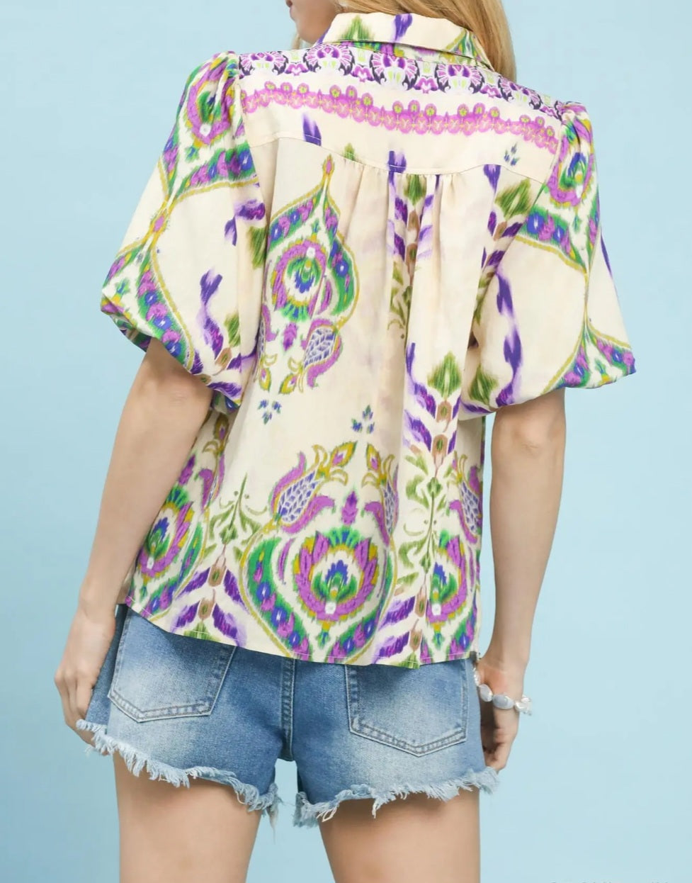Person wearing a colorful patterned shirt and denim shorts on a light blue background