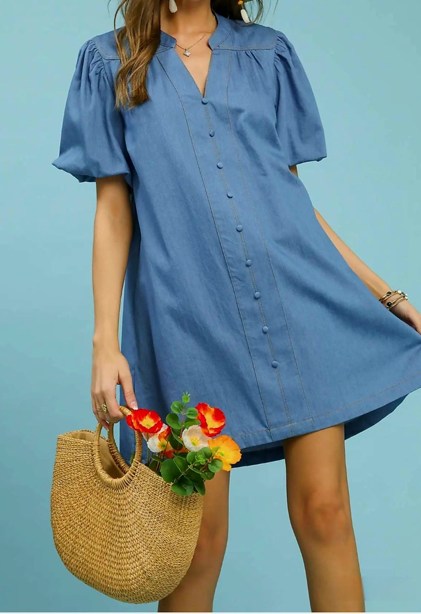Woman wearing a blue dress holding a straw bag with flowers against a blue background