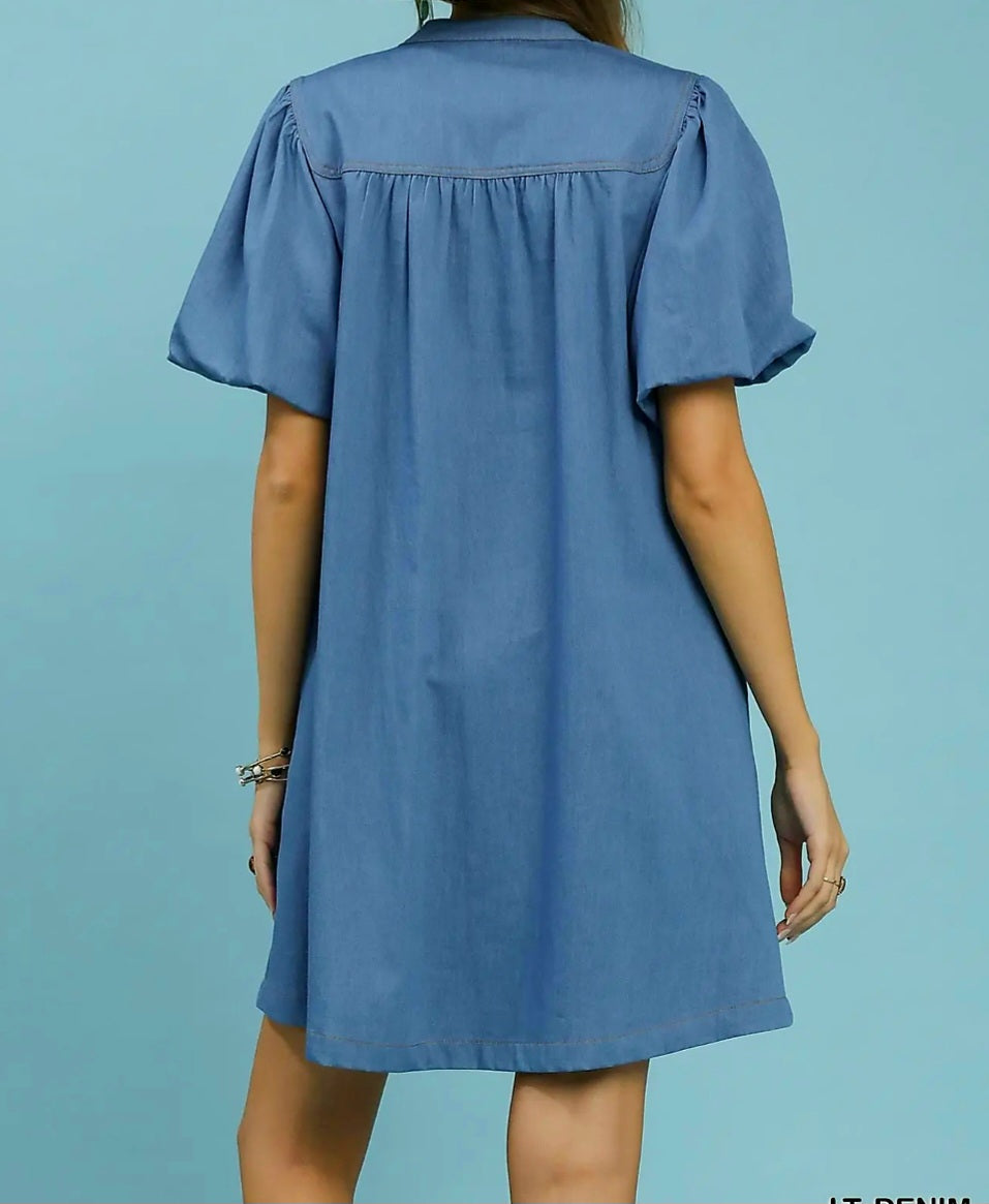Light denim dress worn by a person on a solid blue background