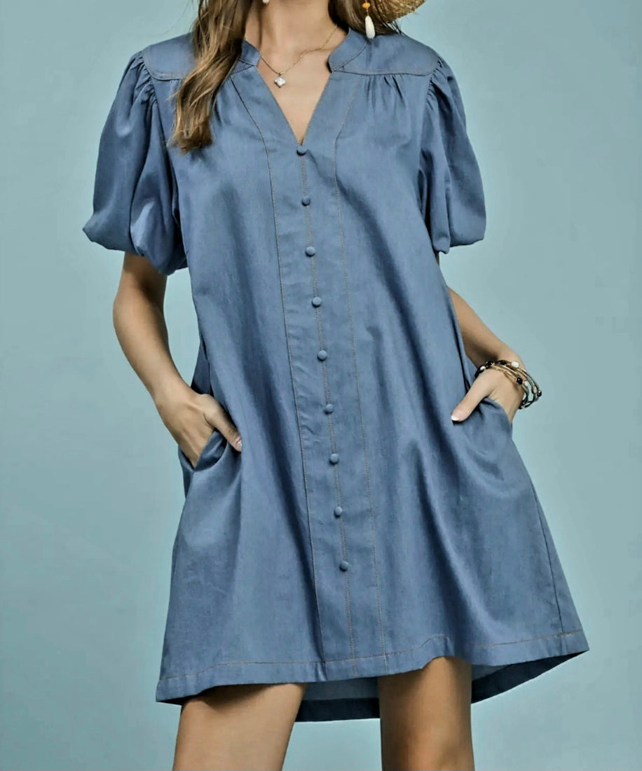 Woman wearing a blue dress with puff sleeves against a gray background