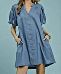 Woman wearing a blue dress with puff sleeves against a gray background