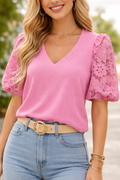Woman wearing a pink blouse with lace sleeves and blue jeans.
