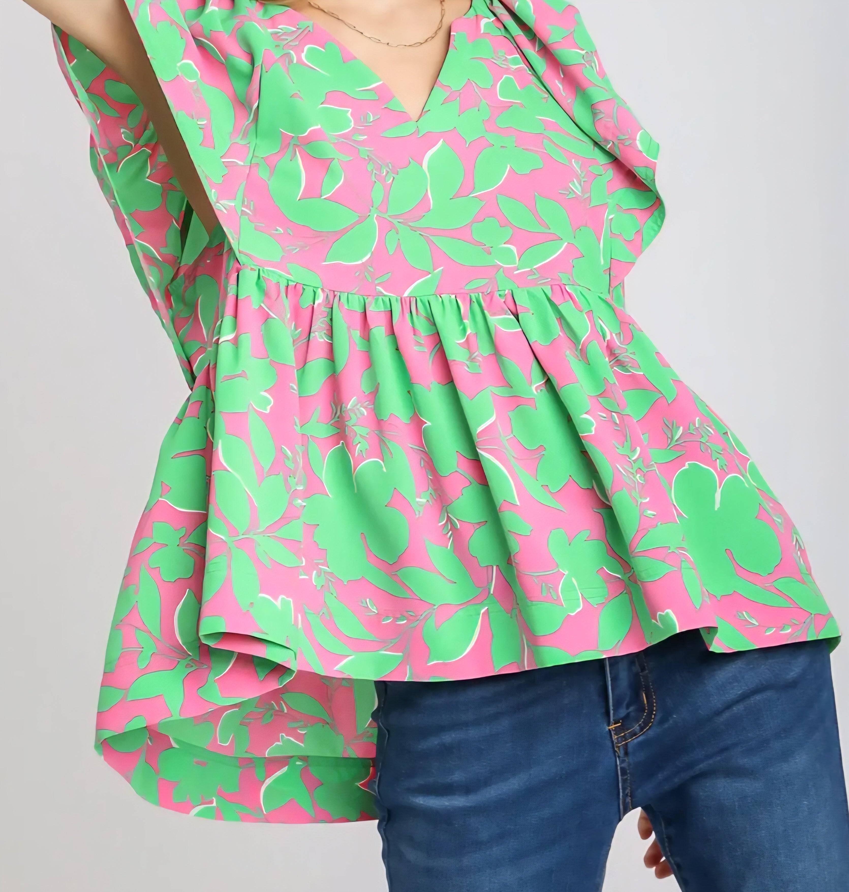 Green and pink floral blouse worn by a person on a gray background