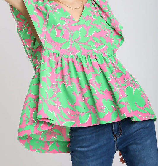 Green and pink floral blouse worn by a person on a gray background